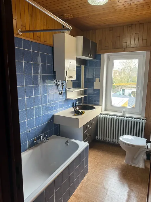 Voor: oude badkamer met ligbad, blauwe tegels en houten plafond